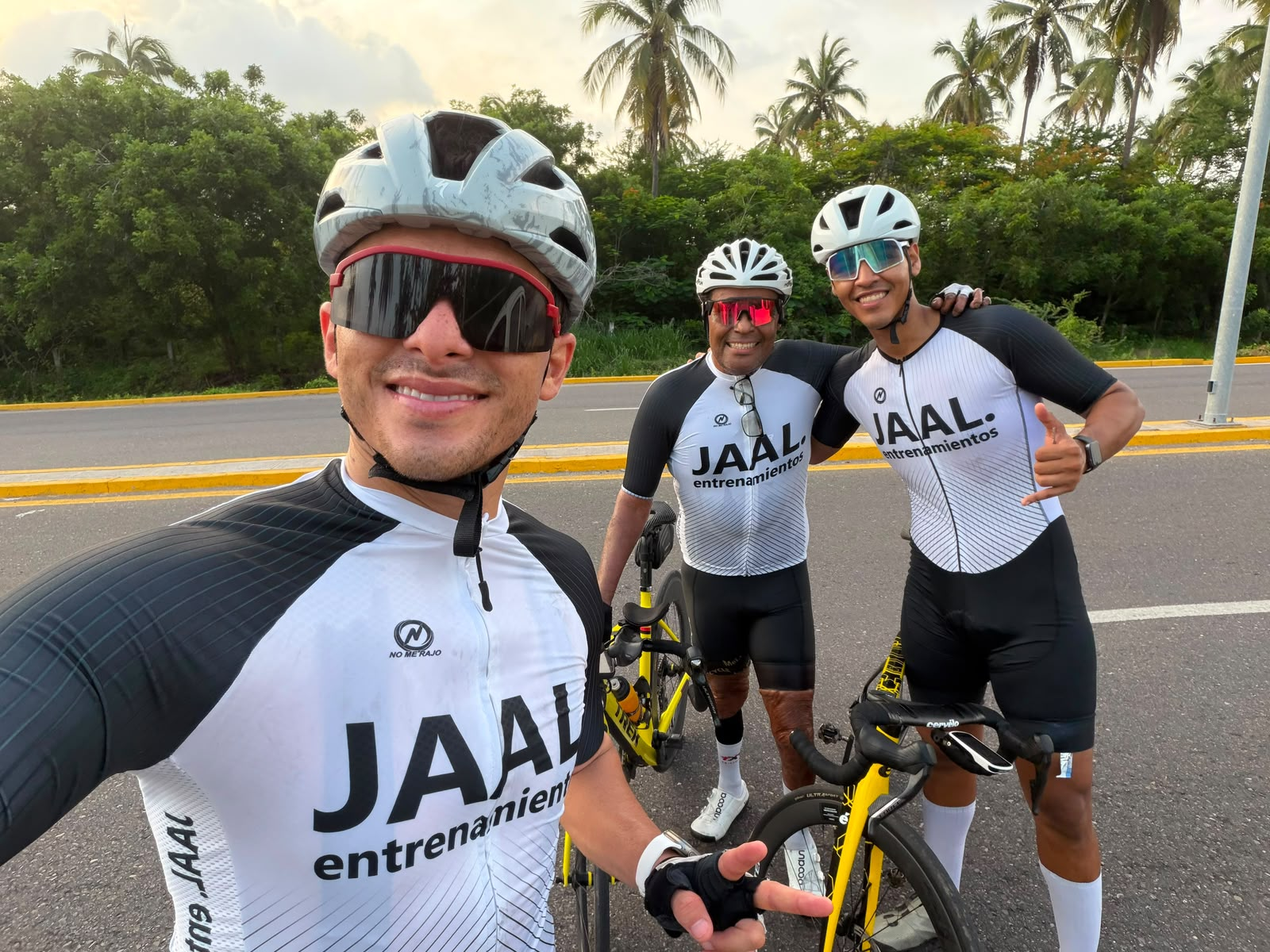 Tres atletas con el jersey JAAL Entrenamientos en una salida de ruta entre palmeras